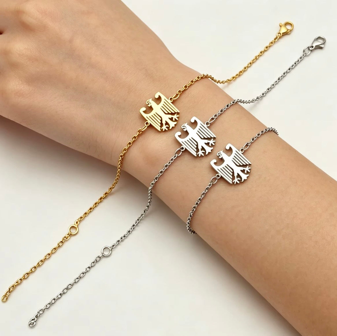 Drei Adler-Armbänder in Gold und Silber an einem Handgelenk