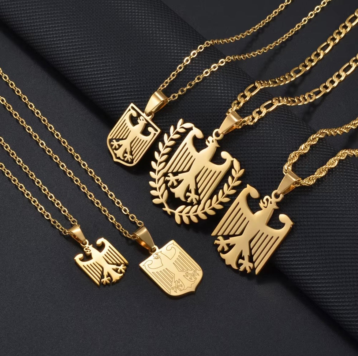 Fünf goldene Adler-Anhänger an verschiedenen Ketten auf dunklem Stoff